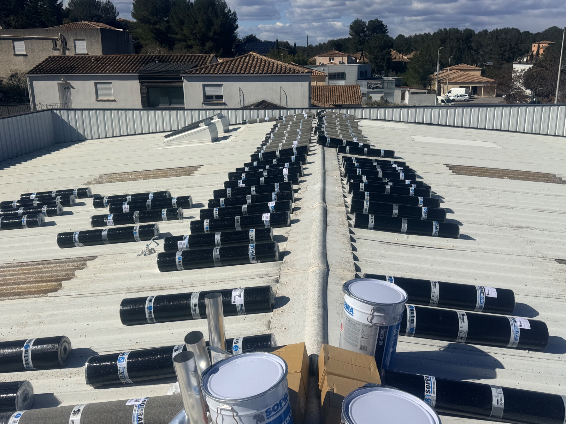Support bac acier existant avec rouleaux de membrane bitumineuse répartis avant la rénovation de l'étanchéité